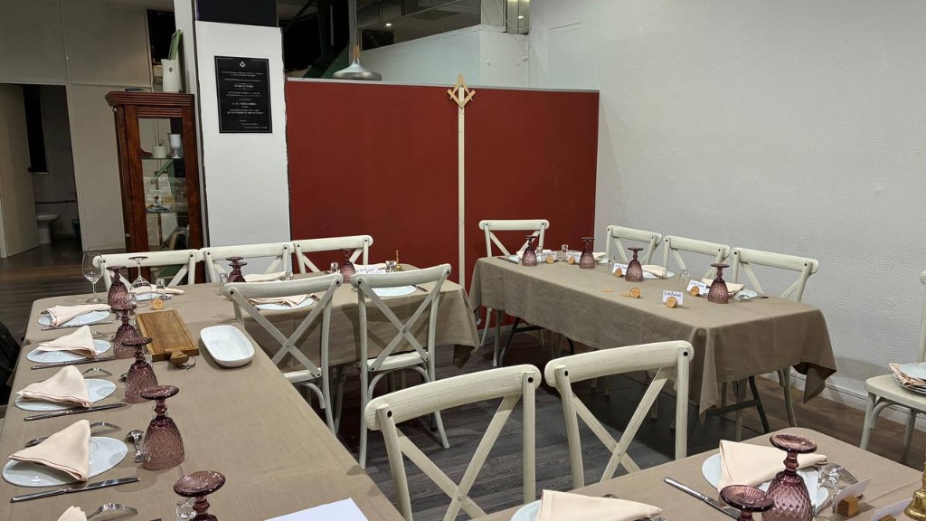 Mesas preparadas para el ágape fraternal en el local de la logia con la escuadra y compás al fondo